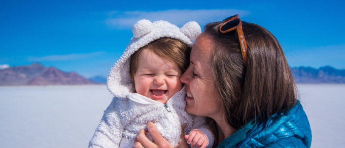 Baby in white bear hoodie with mother giggling in front of salt flats