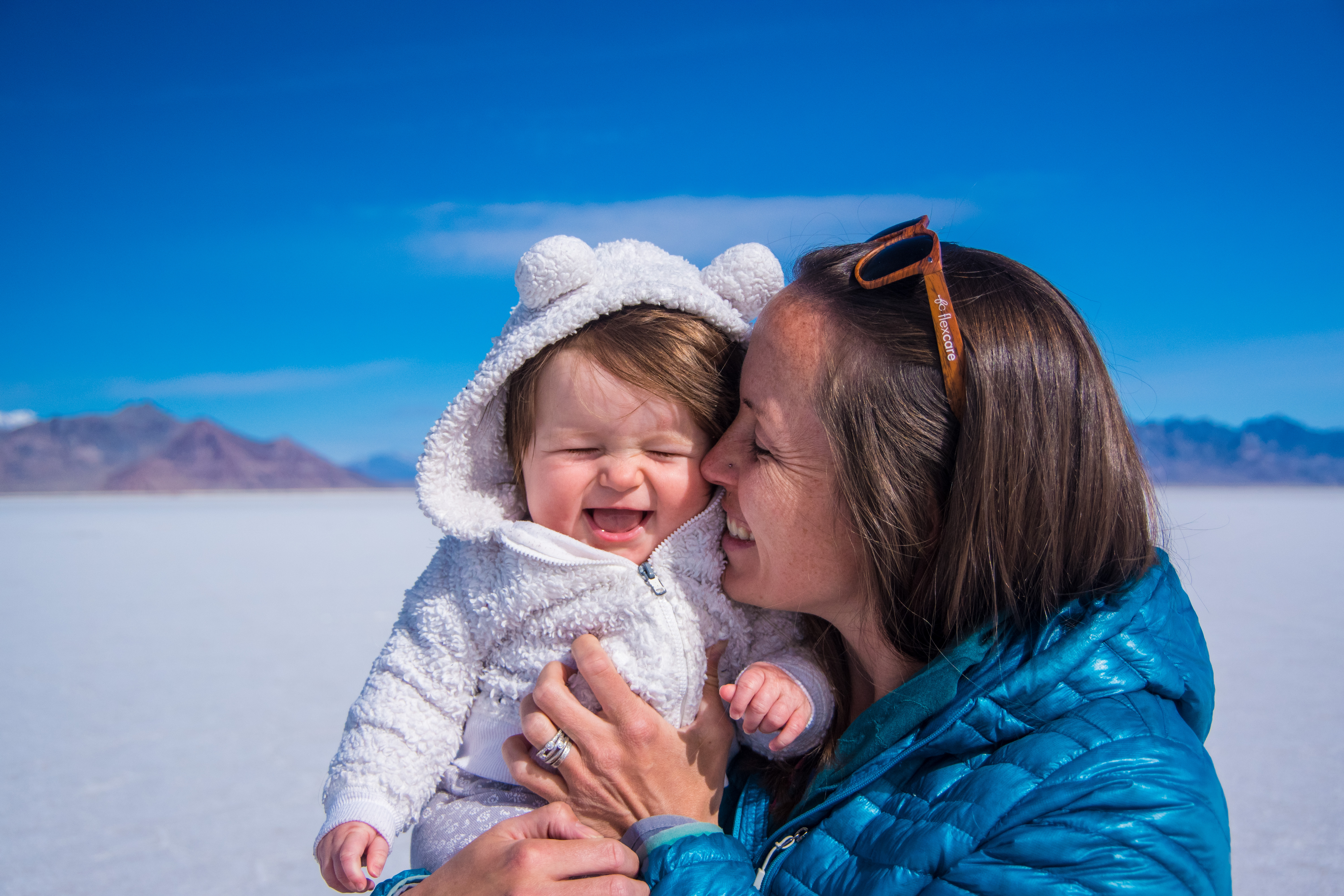 Baby in white bear hoodie with mother giggling in front of salt flats